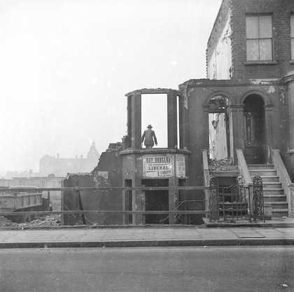 black and white photograph of a man in the doorway of a building which is in ruins, possibly due to bomb damage, post WWII