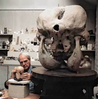 Henry Moore working on the maquette for Atom Piecem alongside an elephants head at his studio in Much Hadlam 1970