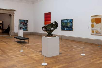 A bronze sculpture on a large pedestal, surrounded by low white wire cord barriers