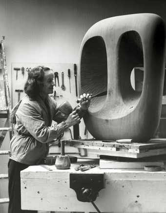 Barbara Hepworth in the Palais studio in 1963 with unfinished wood carving Hollow Form with White Interior Photograph by Val Wilmer, courtesy Bowness, Hepworth Estate