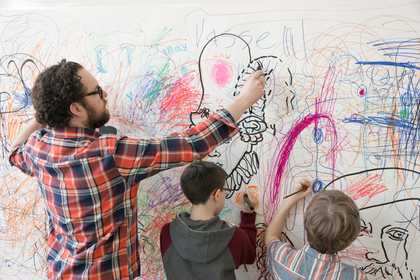 Children and man drawing onto a white wall