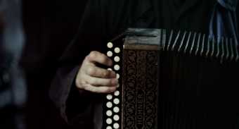 Film still showing a close up of a man playing an accordion