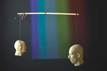 Two moulds of human heads hanging on a mobile with a rainbow behind them