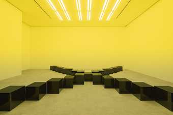 A series of black marble squares places in a cross formation in a room lit with yellow light