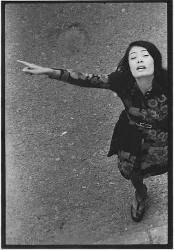 Black and white photo from above of Asian woman with her arms spread, facing up at the photographer