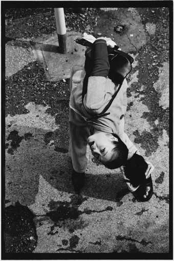 Black and white photograph of Asian woman bending down and looking back up at the photographer above her.