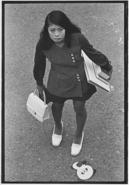 Black and white photo taken from above of Asian woman looking sad carrying an armful of books.