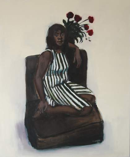 a woman wears a stripey dress and sits on a chair with a vase of roses in the background
