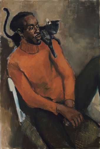 A man in an orange jumper sits with a cat on his shoulder 