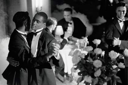 A black and white photograph of a male couple dancing and wearing tuxedos