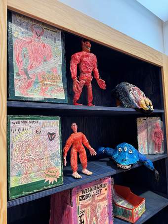 A cabinet with shelves displaying mini creatures next to books.