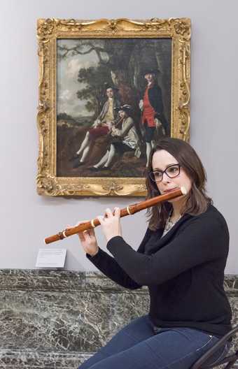 Hannah French poses with a replica of a baroque flute in front of Thomas Gainsborough’s Peter Darnell Muilman, Charles Crokatt and William Keable in a Landscape c.1750