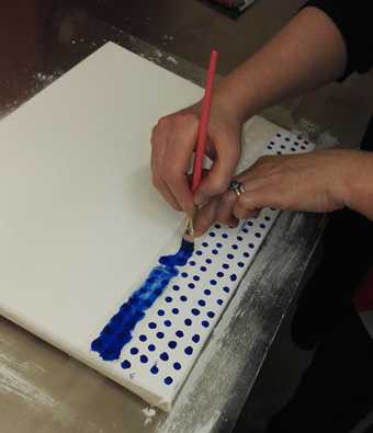 Paintings conservator Rachel Barker applying blue oil paint through a stencil to recreate the Ben Day dots on Whaam! for a mock-u-