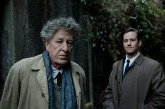 film still of Geoffrey Rush in a suit staring at the camera with a man behind him