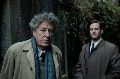 film still of Geoffrey Rush in a suit staring at the camera with a man behind him