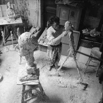 Giacometti working on the plaster sculpture for "L'homme qui marche" ("The Walking Man"), 1958