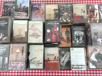Cassettes of Koh Nguang How's performance art audio recordings are lined up on a gingham table cloth 