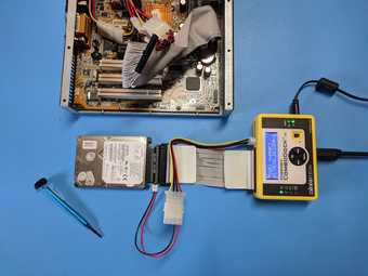 A dismantled computer hard drive, cables and a screwdriver on a blue tabletop