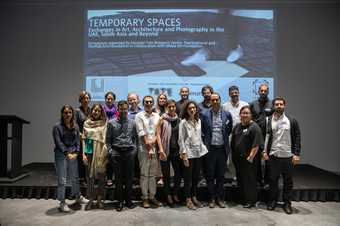 A group photograph of contributors to the ‘Temporary Spaces’ symposium, posing together in front of a projected slide showing the title of the event