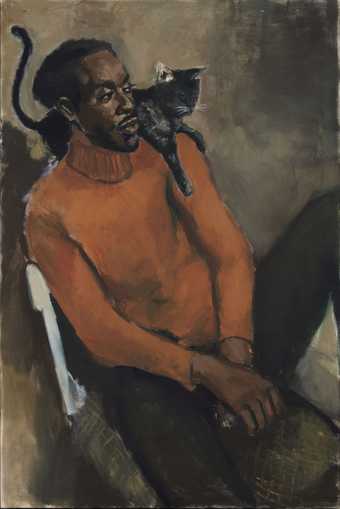 a man in an orange jumper sits on on a chair with a cat on his shoulder