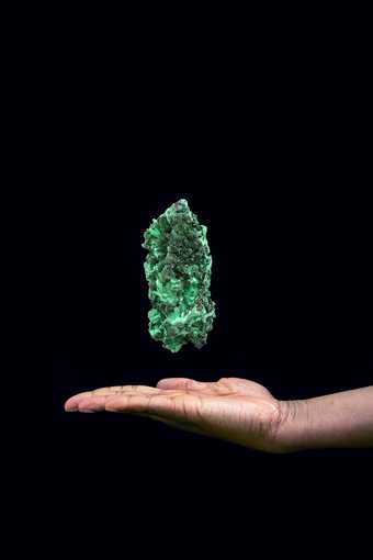 Photograph of a hand with a green precious stone floating above it against a black background