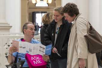 a staff member in a wheelchair shows two visitors a map in Tate Britain