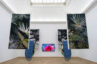 A photograph of an installation which features hanging material and a tv screen in the centre