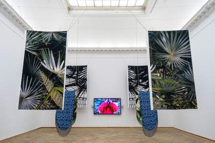 A photograph of an installation which features hanging material and a tv screen in the centre