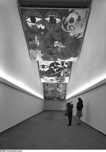Installation view of works by Ernst Wilhelm Nay at Documenta 3 in Kassel curated by Arnold Bode 1964 photograph of a hallway with paintings hung from the ceiling 