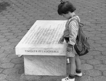 A little girl looks at a marble bench engraved with text