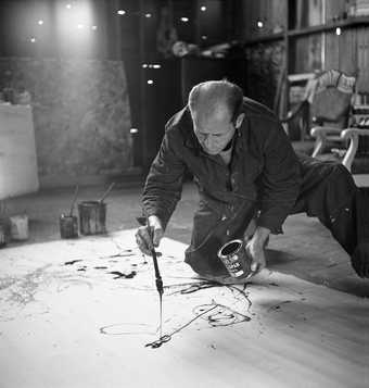 Painter Jackson Pollock working in his studio, dropping paint onto canvas