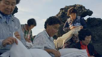 Five people outside on a rocky landscape holding fabrics on their laps