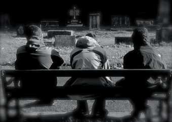 Black and white photograph of three boys in hoodies sitting on a bench