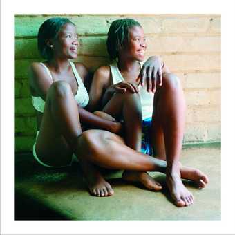 A colour photograph of two women sat together on the floor