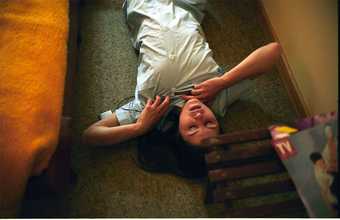 Colour film still of a woman lying down on a carpet wearing a buttoned up pastel blue green dress