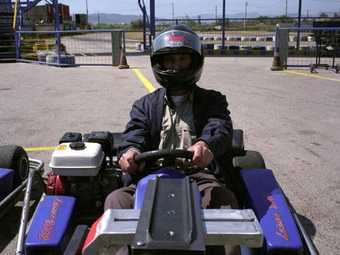 Film still of a man in a go cart on a track facing the camera, wearing a helmet