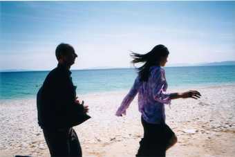 Colour film still of a man and woman mid run on a sunny beach