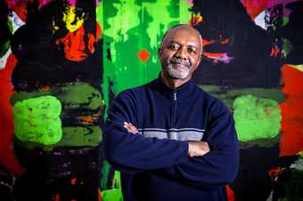 Photograph of a Kerry James Marshall looking at the camera in front of an abstract green and red painting
