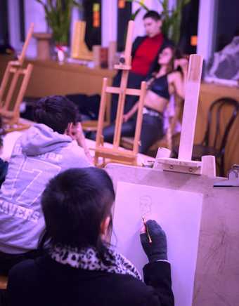 people sit with easels and sketch two life drawing models in front of them