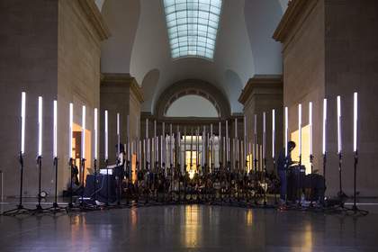Two people playing instruments to the backdrop of vertical white light tubes