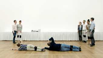 Group of people in white gallery space with two people lying on the ground