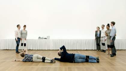 Group of people in white gallery space with two people lying on the ground