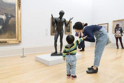a boy and his mother stand in Tate Britain in front of a sculpture of a figure