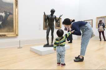 a boy and his mother stand in Tate Britain in front of a sculpture of a figure