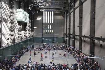 Crowd sit around the turbine hall with some dancers in the middle