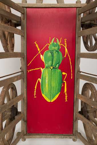 view of a wooden cart painted red with a painting of a bright green beetle