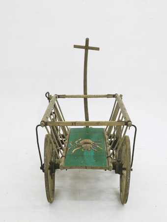 view of a wooden cart with the chassis painted green and featuring a painting of a large hairy spider