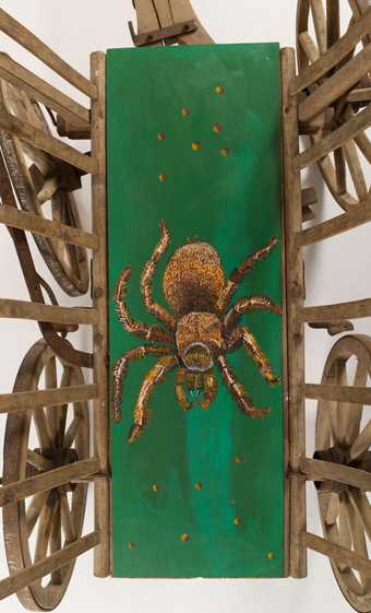 view of a wooden cart with the chassis painted green and featuring a painting of a large hairy spider