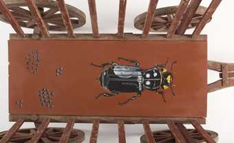 view of a wooden cart with the chassis painted brown and featuring a painting of a black beetle