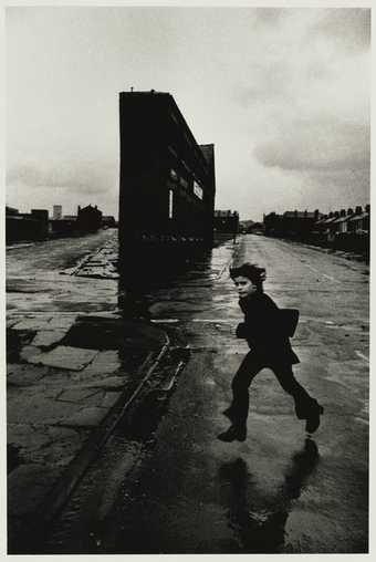 Black and white photo of a young boy running by a building